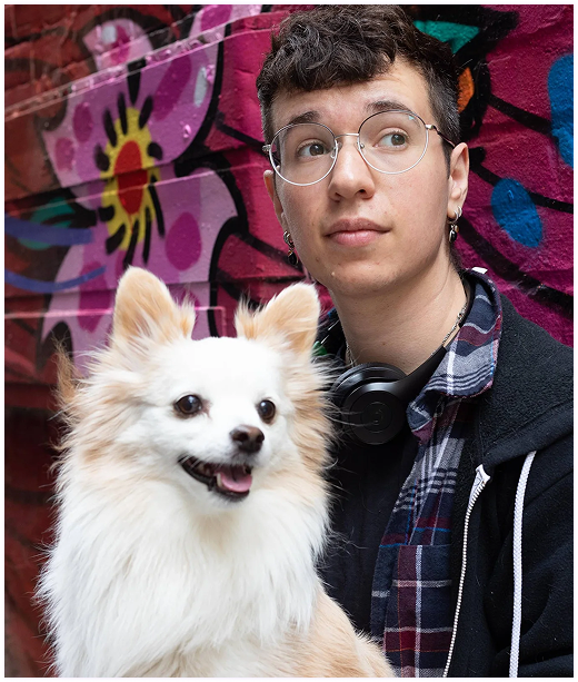 person with short dark hair looking past the camera with a small white dog in their lap